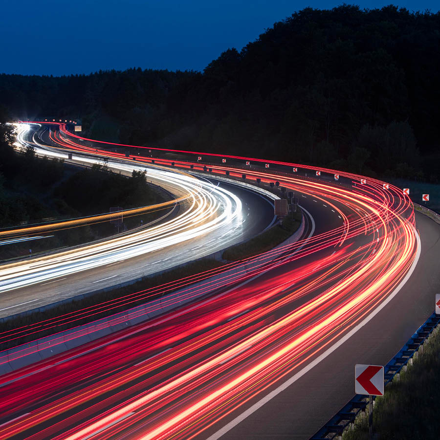 Nachtaufnahme einer Autobahn mit Lichtspuren des Verkehrs als Symbol für moderne Straßen- und Verkehrsinfrastruktur.