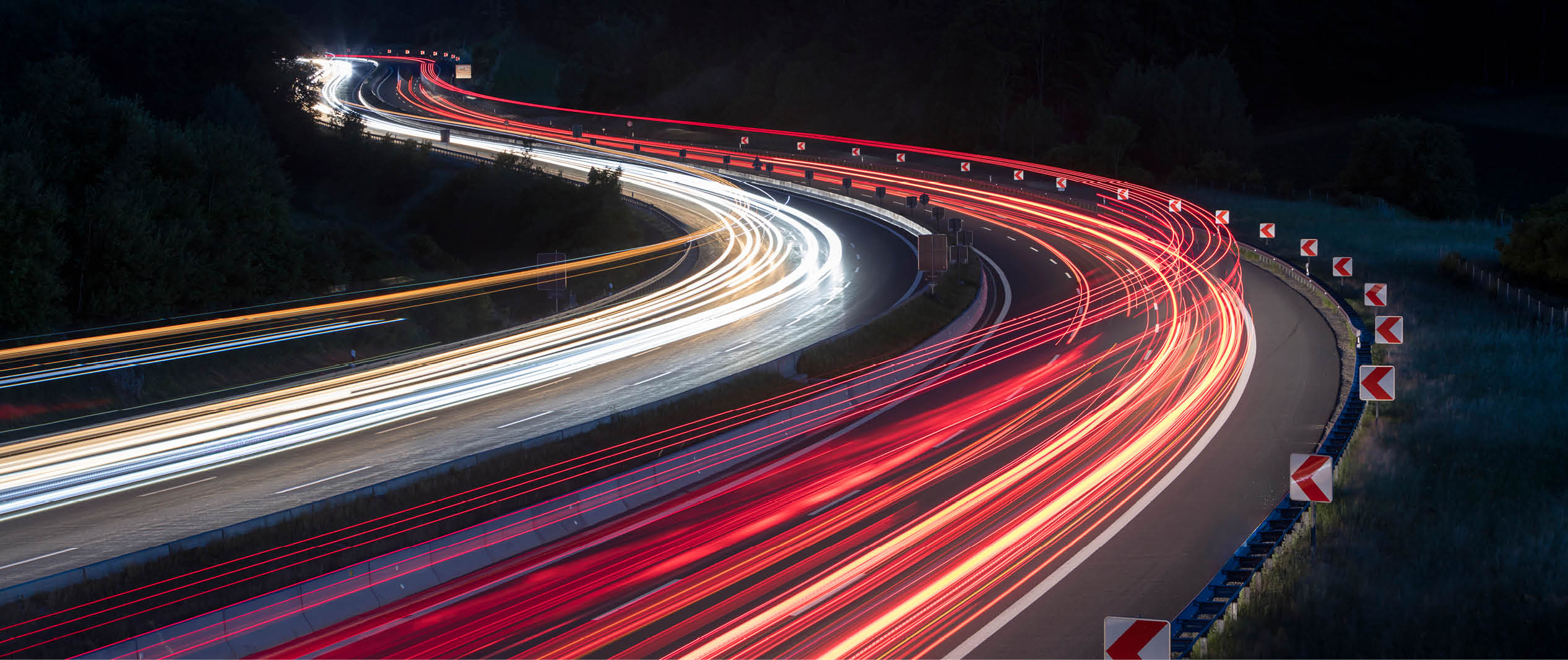 Nachtaufnahme einer Autobahn mit Lichtspuren des Verkehrs als Symbol für moderne Straßen- und Verkehrsinfrastruktur.